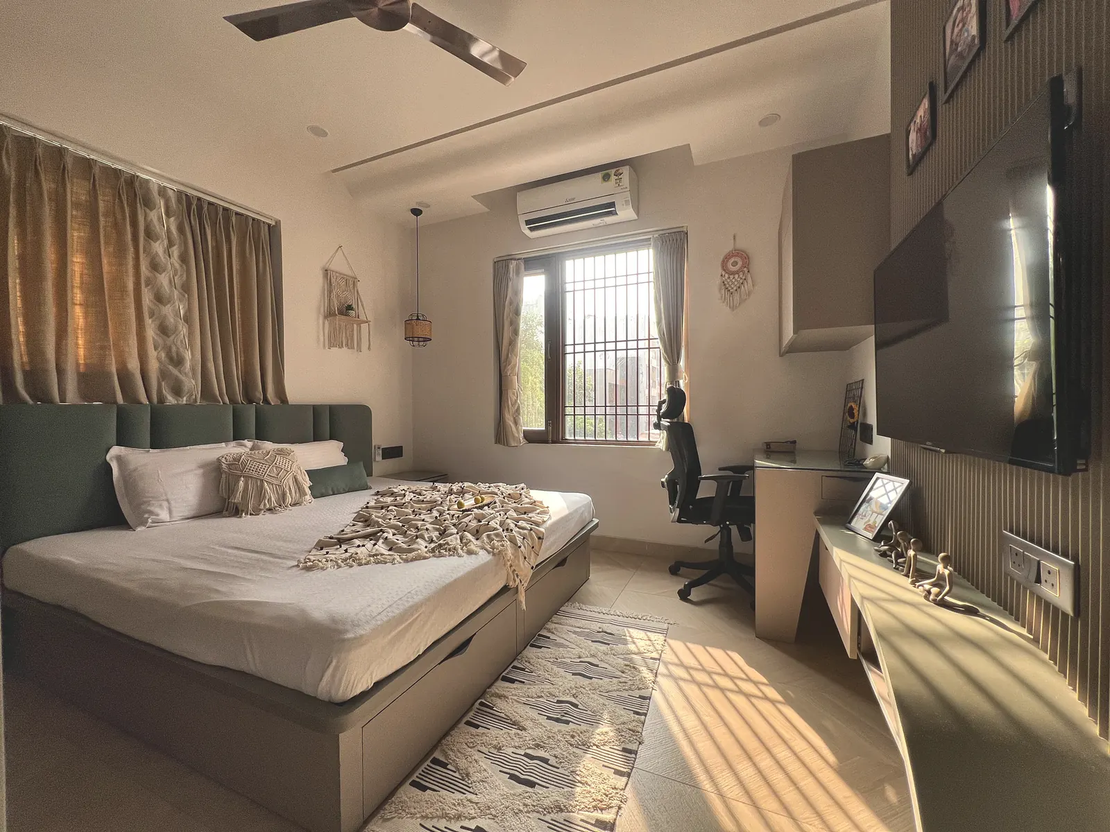Sunlit bedroom with a sage-green tufted headboard, macrame wall hanging, rattan pendant light